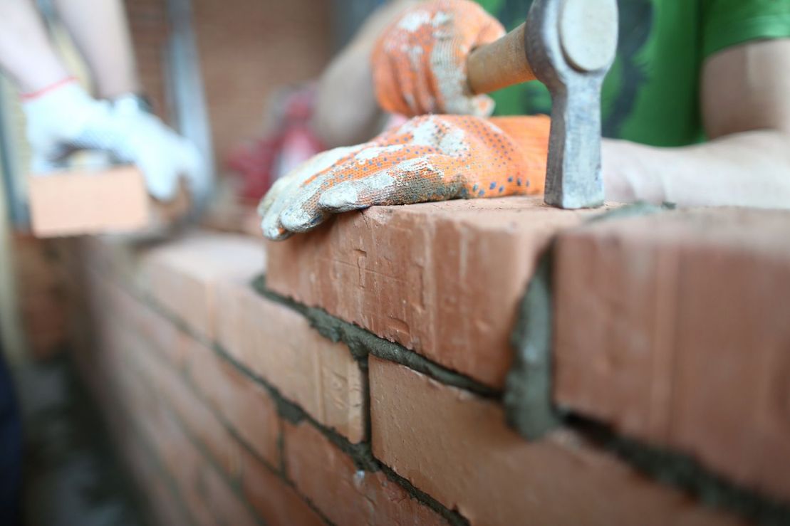 manos de albañil con martillo colocando muro de ladrillo 